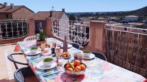 A dining table set outdoors with a view of a residential area and hills in the background.