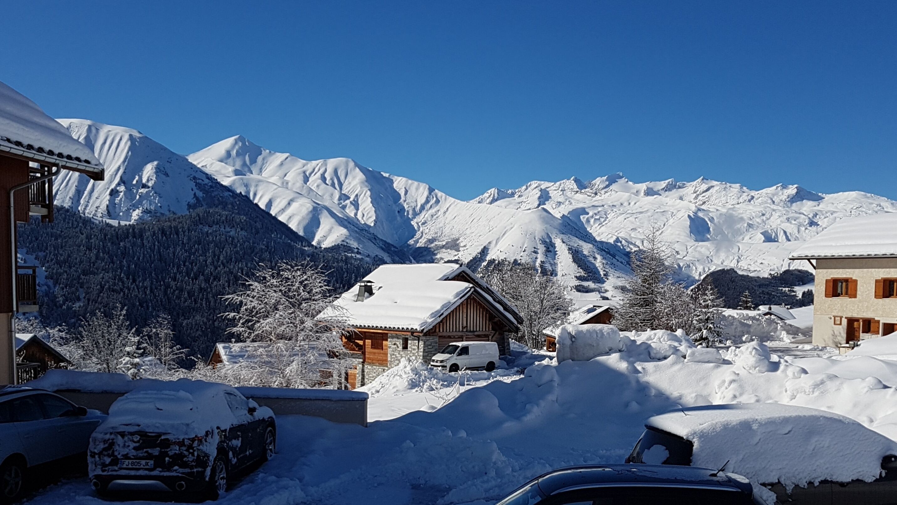 En snötäckt bergsby med traditionella trähus, en klarblå himmel och en snötäckt bil i förgrunden.