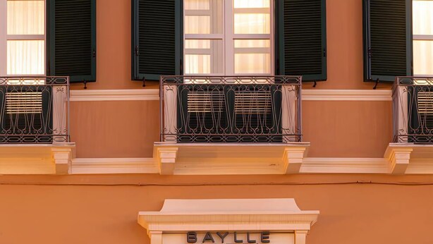 Fachada de hotel con un letrero que dice "Baylle Hotel", con balcones de barandilla metálica y contraventanas.