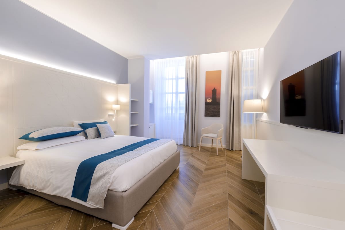 A modern hotel room with a large bed, a TV, a desk, and a chair.