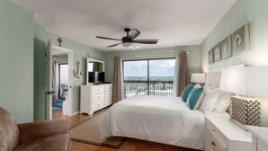 Un dormitorio con cama, ventilador de techo, cómoda, televisor y vistas al exterior.