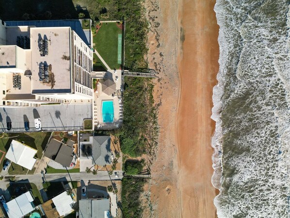 Vista aérea de una propiedad costera con piscina, zona de estacionamiento y playa.