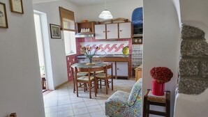 Eine Küche mit Esstisch, Stühlen und einer Couch. Es gibt einen Herd, ein Waschbecken und ein Fenster mit Jalousien.