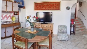 Ein Essbereich mit Holztisch, Stühlen und einer Vase mit Blumen. Ein Fernseher ist über dem Tisch an der Wand befestigt.