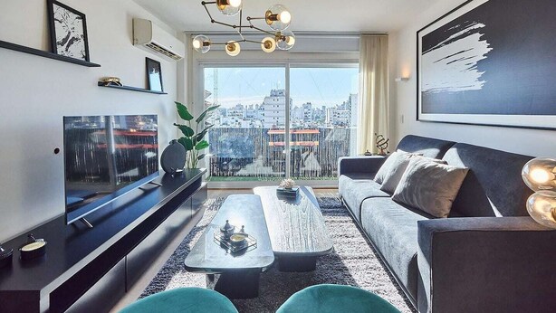 Un soggiorno moderno con una grande televisione, un divano, un tavolino da caffè e vista sulla città tramite ampie finestre.