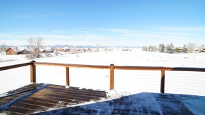 A wooden deck with a metal railing overlooking a snowy landscape with houses and trees.