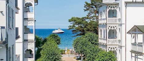 Uma rua costeira com edifícios brancos, um barco ao longe e um caminho para pedestres.