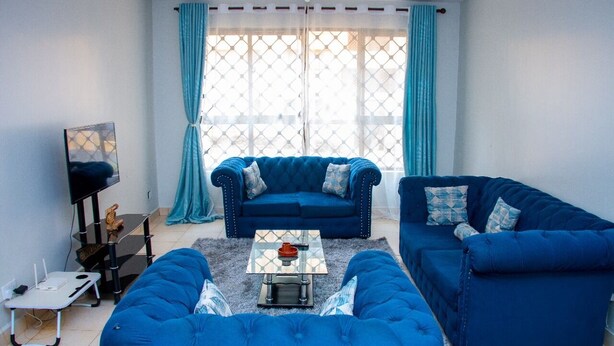 A living room with a blue sofa set, a glass coffee table, and a TV on a stand. - Honey Dew Stays (Athi River)