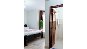 A bedroom with a bed, a potted plant, a wooden door, and a bathroom mat. - Honey Dew Stays (Athi River)