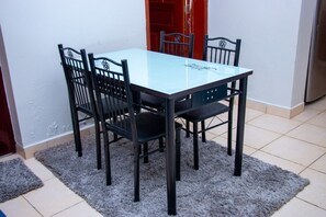 A dining table with four chairs, a glass top, and a rug on a tiled floor.