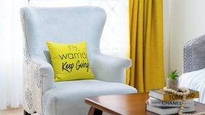 A light blue armchair with a yellow pillow that reads "Warrior Keep Going." - Honey Dew Stays (Athi River)
