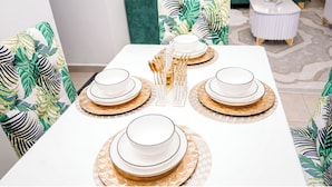 A dining table set with white plates and gold accents, surrounded by green upholstered chairs with leaf patterns. - Honey Dew Stays (Athi River)