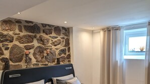 Ein modernes Schlafzimmer mit einer Steinwand, einem großen Bett mit grauer Bettwäsche und einem Fenster mit Vorhängen.
