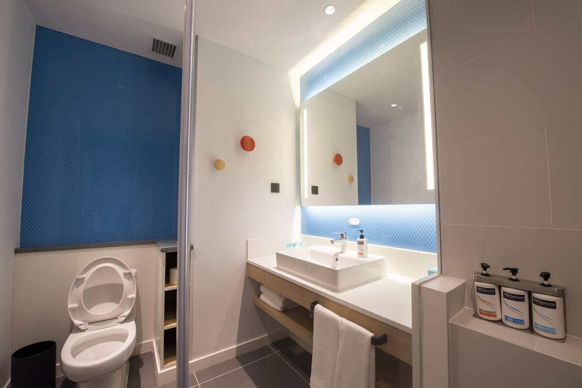 A modern bathroom with a white toilet, a large mirror, a white sink, and a towel rack.