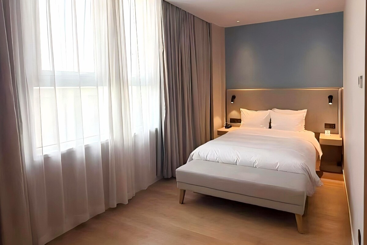 A modern hotel room with a large bed, a nightstand, and a wall-mounted lamp.