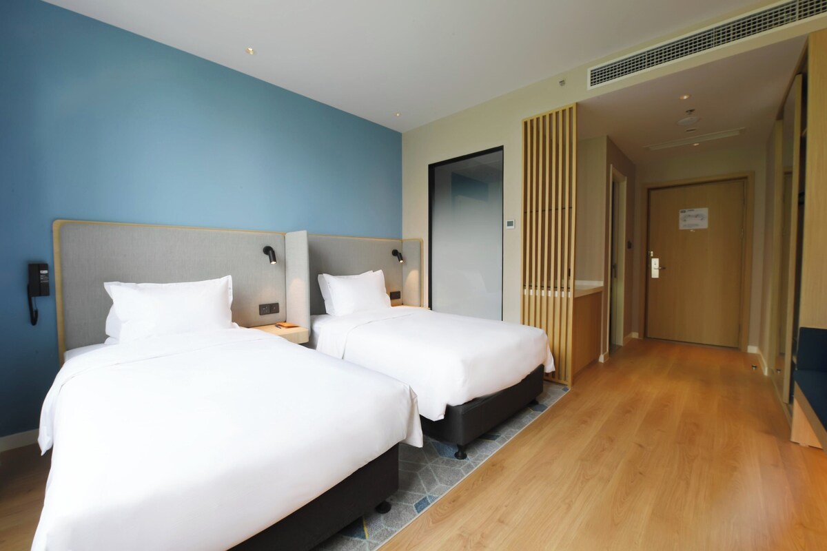 A hotel room with two beds, a wooden floor, and a blue wall.