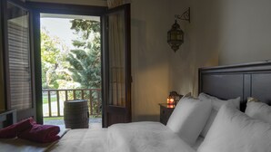 A bedroom with a large bed, a nightstand with a lantern, and a view of a balcony with trees. - Dandy Villas Amfiklia (Amfikleia-Elateia)