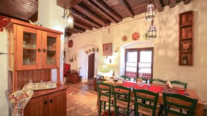 A traditional dining room with a wooden table, green chairs, and a red rug. There is a wooden cabinet with glass doors and a hanging lantern above the table. - Dandy Villas Amfiklia (Amfikleia-Elateia)
