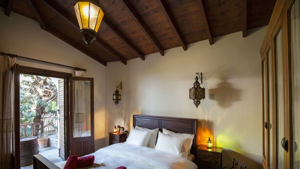 A bedroom with a wooden ceiling, a large bed with white linens, two bedside lamps, and a view of a garden through an open door. - Dandy Villas Amfiklia (Amfikleia-Elateia)