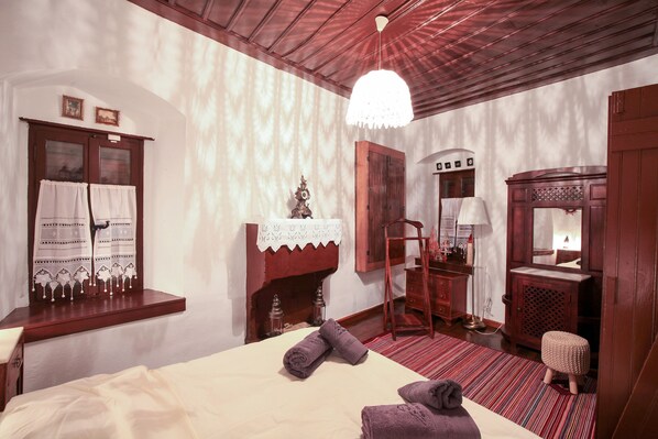 Un dormitorio con cama, cómoda de madera, espejo, taburete pequeño y ventana con cortinas.