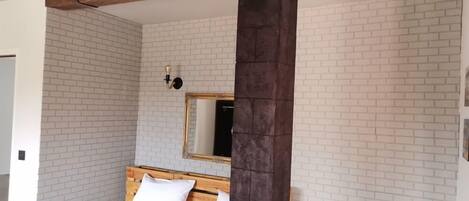 A bedroom with a wooden headboard, white brick walls, a large mirror, and a dark pillar.