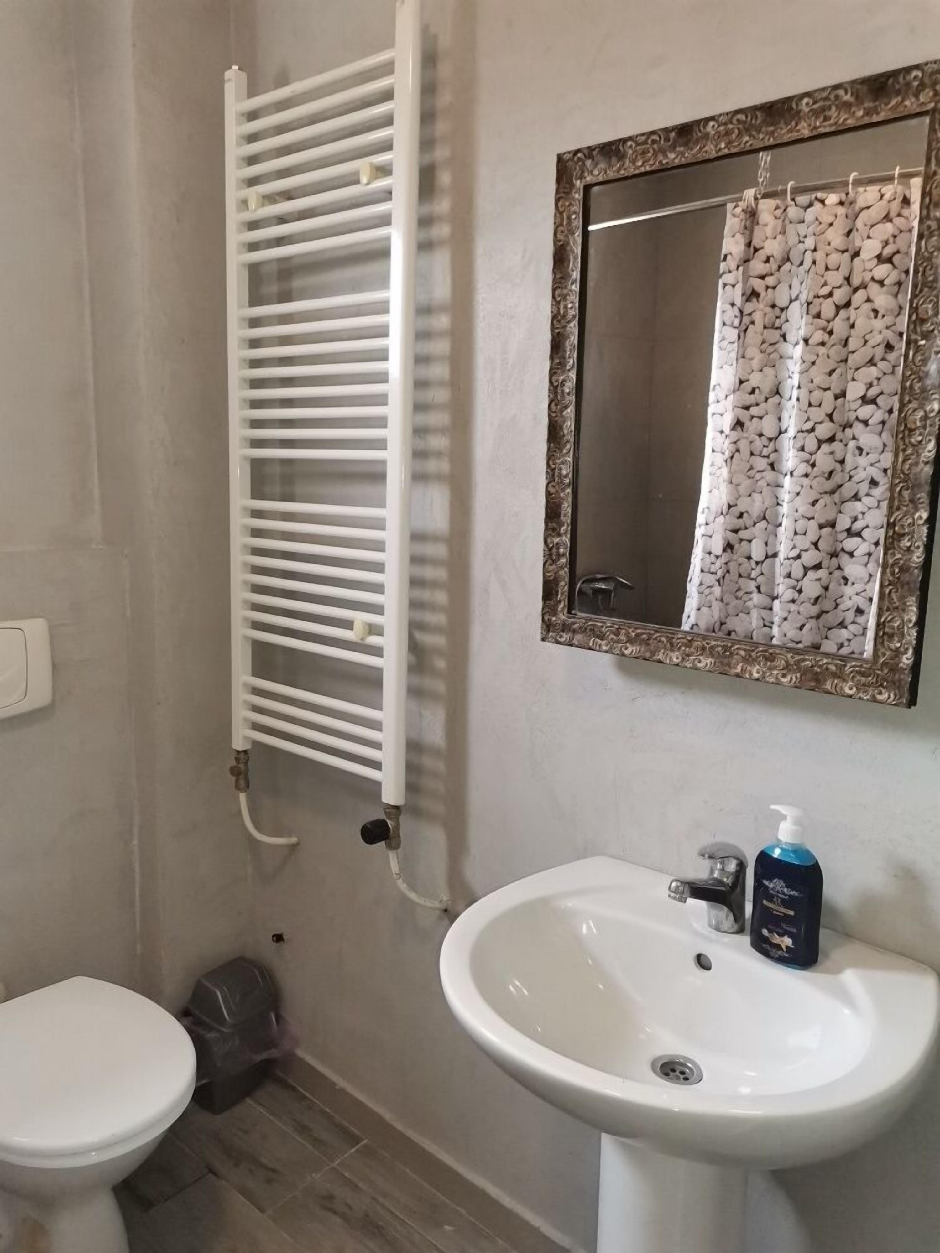 A bathroom with a white toilet, a white sink with a mirror above it, and a white towel rack.