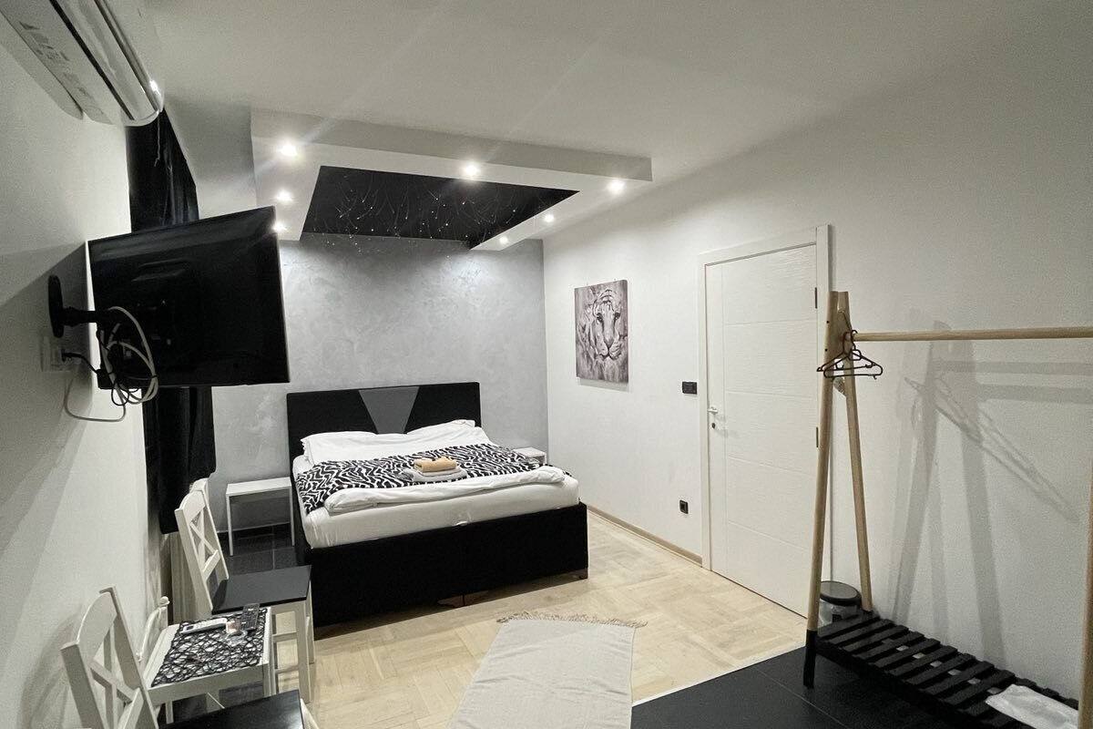A modern bedroom with a bed, a desk, a chair, a TV, and a door.