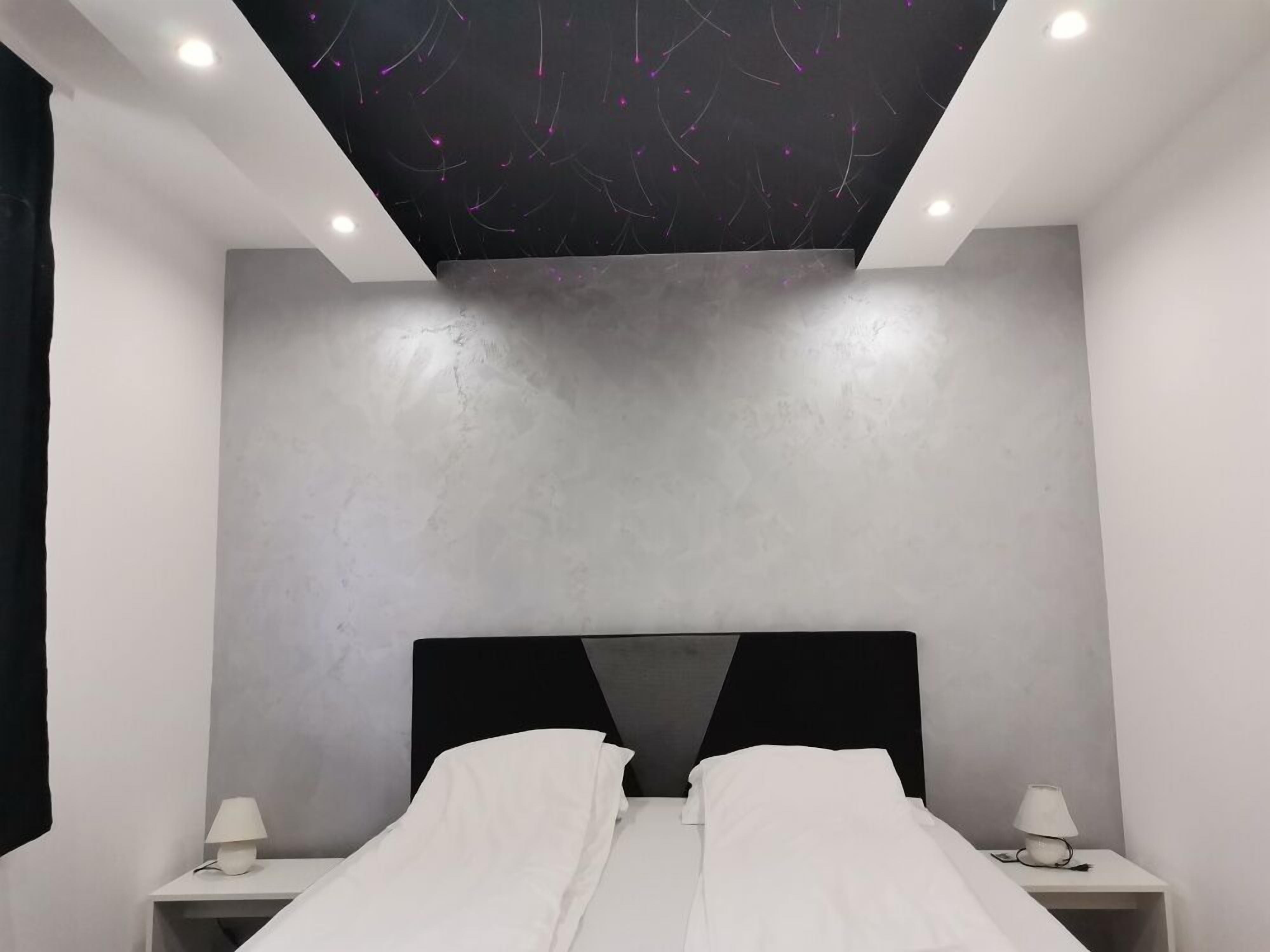 Une chambre moderne avec un lit, deux tables de chevet et un plafond agrémenté d’un luminaire original.
