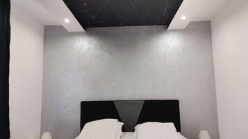 Une chambre moderne avec un lit, deux tables de chevet et un plafond agrémenté d’un luminaire original.