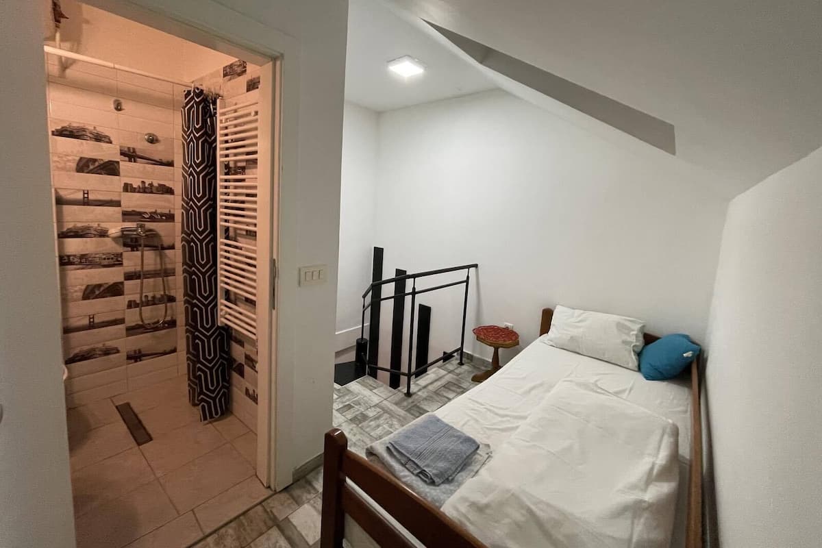 A bedroom with a bed, a bedside table, a chair, and a patterned shower curtain.