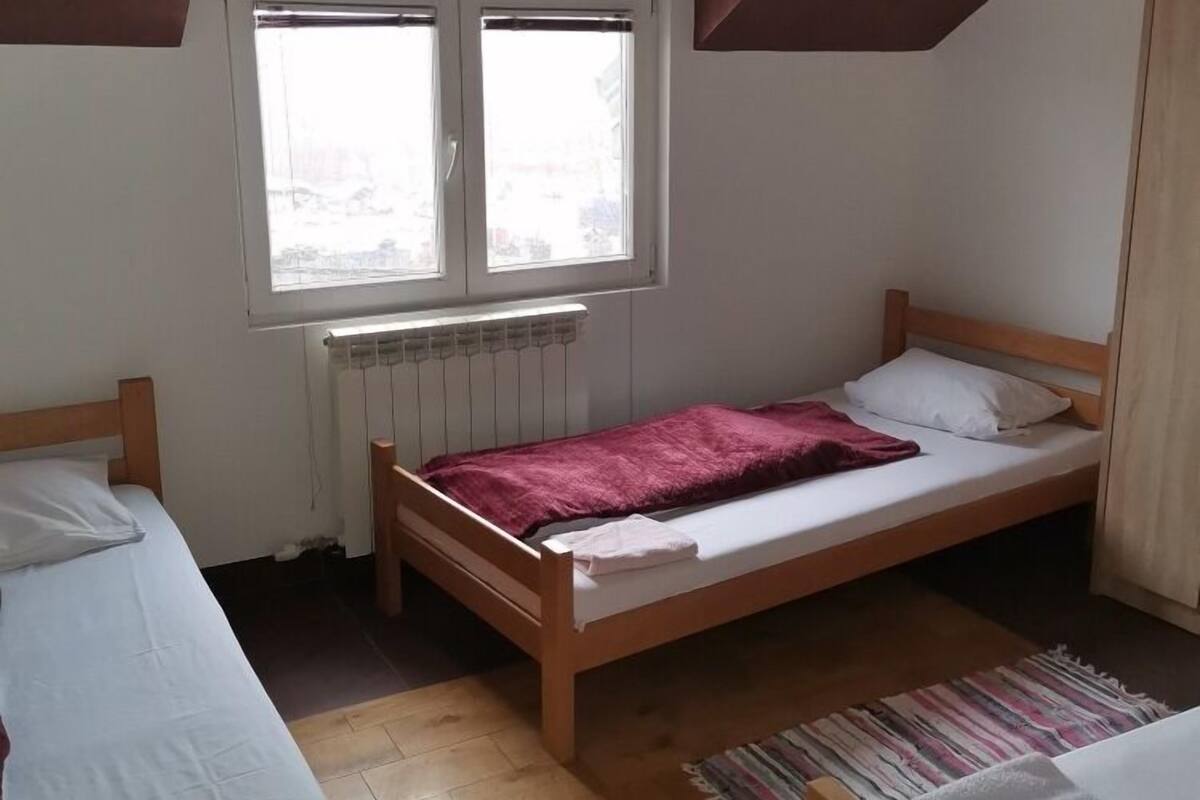 A dormitory room with two single beds, a window, a radiator, and a sloped ceiling.