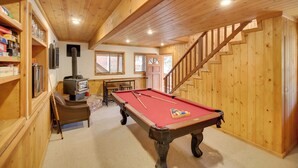 Un intérieur en bois avec une table de billard, une cheminée et un escalier.