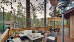 Une terrasse dotée de mobilier d’extérieur, comprenant une table et des chaises, entourée de grands arbres et offrant une vue sur une maison.
