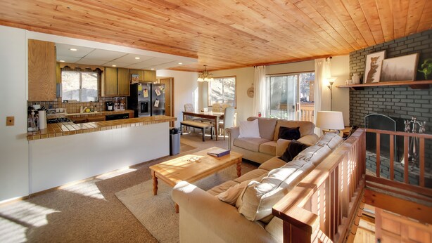 Un vaste espace de vie doté d’un plafond en bois, d’un canapé, d’une table basse et d’une cheminée.