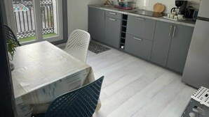 Cozinha compacta com armários cinza, uma mesa de jantar e janela com vista para a rua.