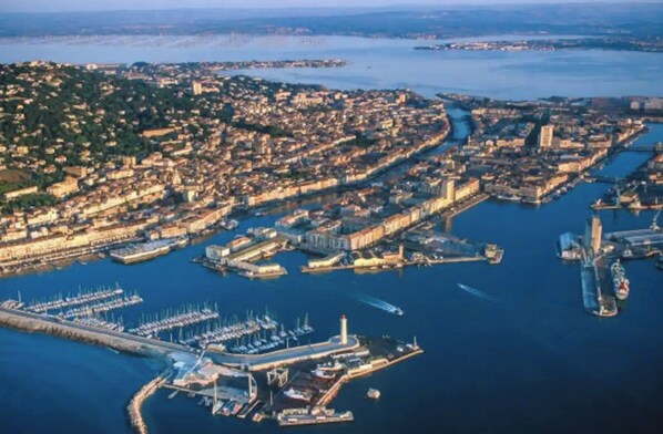 Vue aérienne d’une ville côtière, avec un port de plaisance, une zone urbaine densément peuplée et un phare imposant.