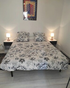 A bedroom with a floral bedspread, two bedside tables with lamps, and a poster on the wall.