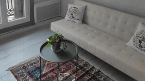 Sala de estar com sofá branco, tapete estampado e uma pequena mesa redonda com uma planta.
