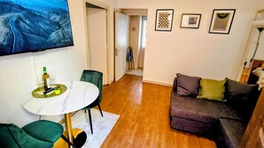 Ein Wohnzimmer mit Fernseher, eine Essecke mit Tisch und Stühlen, eine Couch und ein Flur, der in einen weiteren Raum führt.