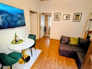 Een woonkamer met een televisie, een eethoek met een tafel en stoelen, een bank en een gang die naar een andere kamer leidt.