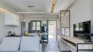 A modern kitchen with a dining area, built-in appliances, and a large TV. - Serenity Suites Sea View 1 (Zacharo)