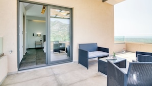 A balcony with wicker furniture, a glass door leading to a room, and a view of the sea. - Serenity Suites Sea View 1 (Zacharo)