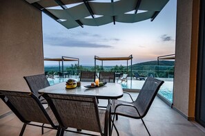 A dining area with a table and chairs, overlooking a pool and a scenic view.
