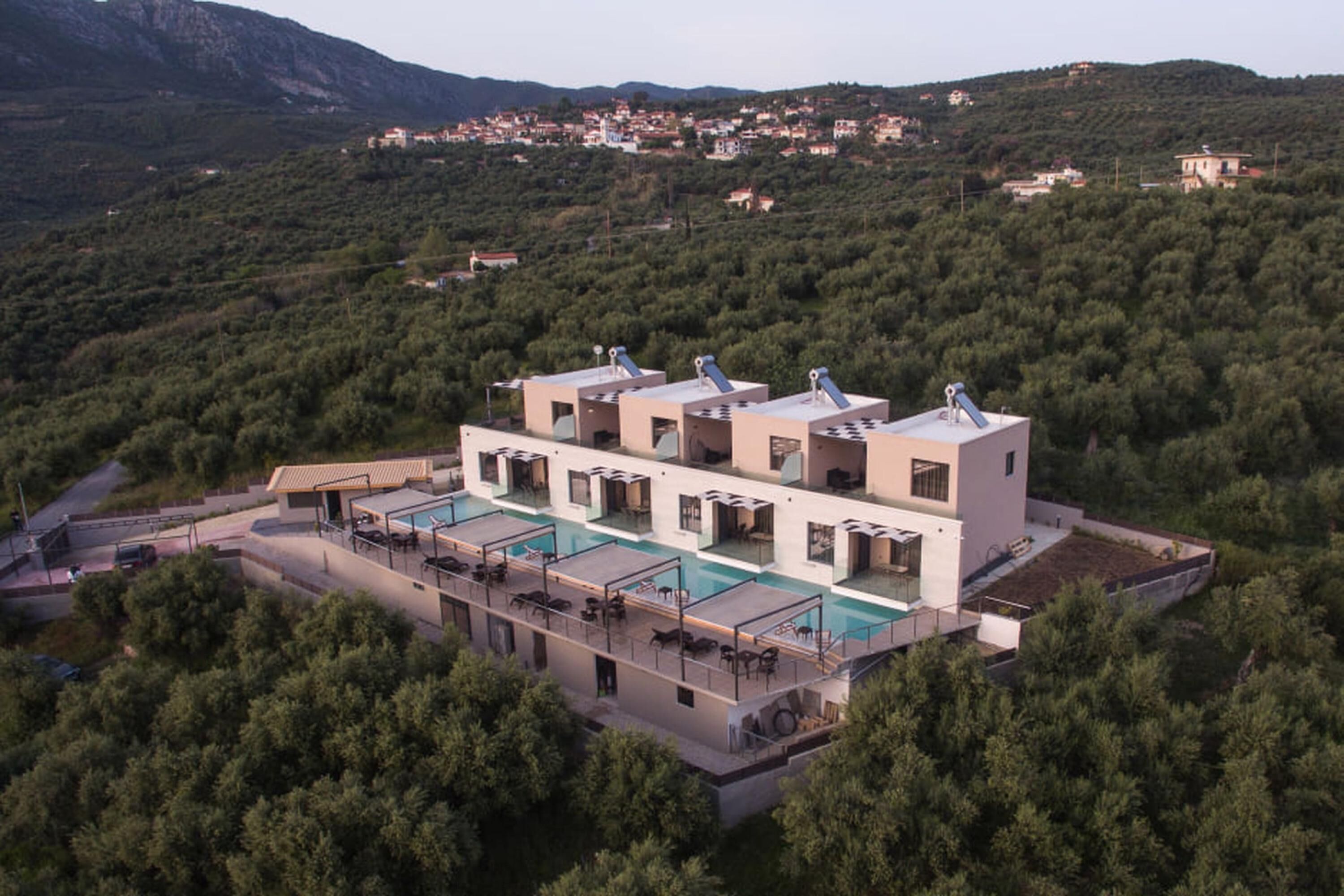 A modern villa with a large pool, multiple guest rooms, and a view of a hillside village.
