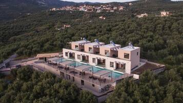 A modern villa with a large pool, multiple guest rooms, and a view of a hillside village.