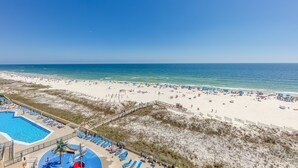 A beach resort with a swimming pool, beach umbrellas, and a sandy beach.