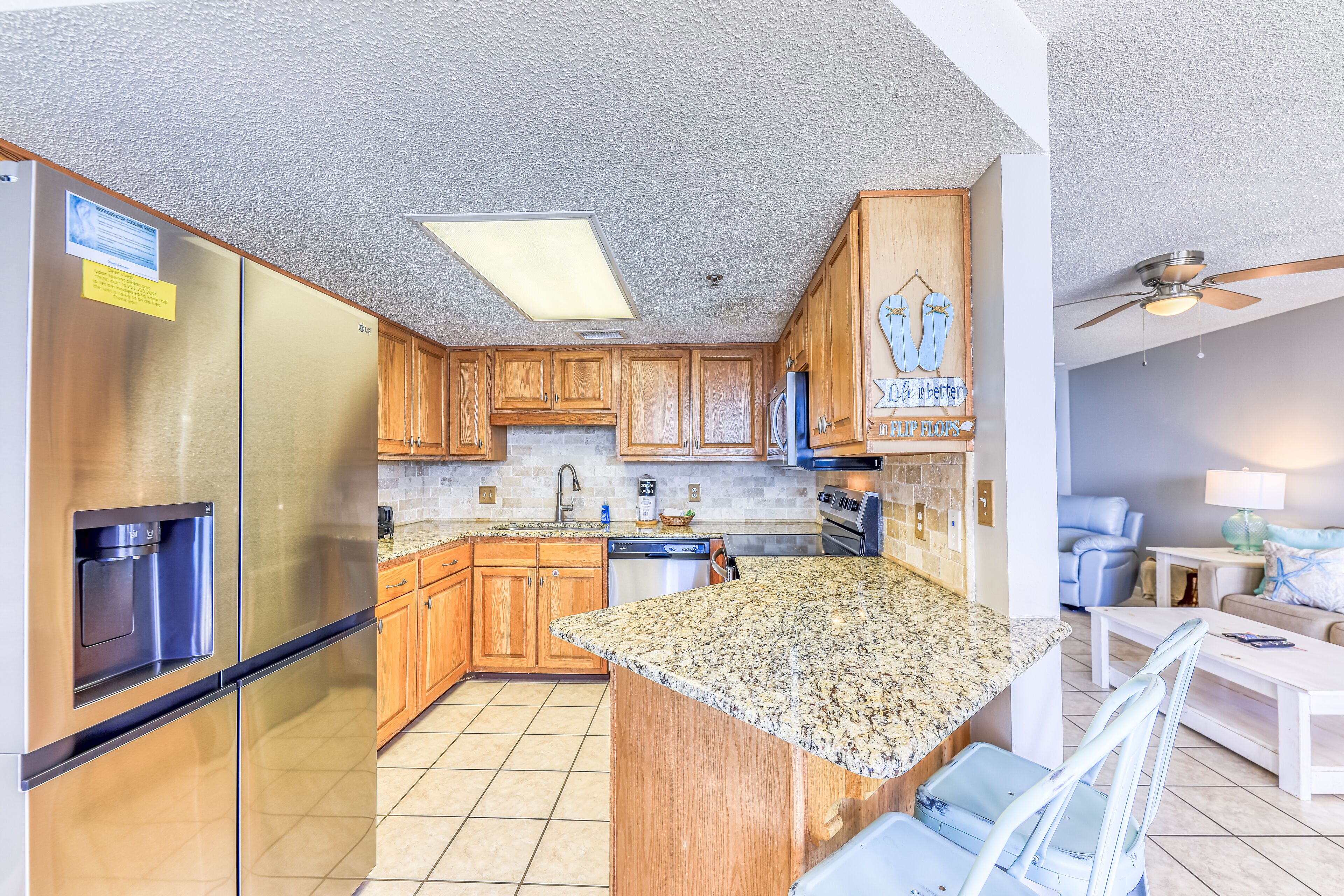 A kitchen with wooden cabinets, a stainless steel refrigerator, a granite countertop, and a ceiling fan.