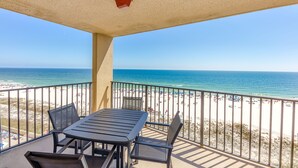 A balcony with a table and chairs overlooking a beach with a clear view of the ocean.