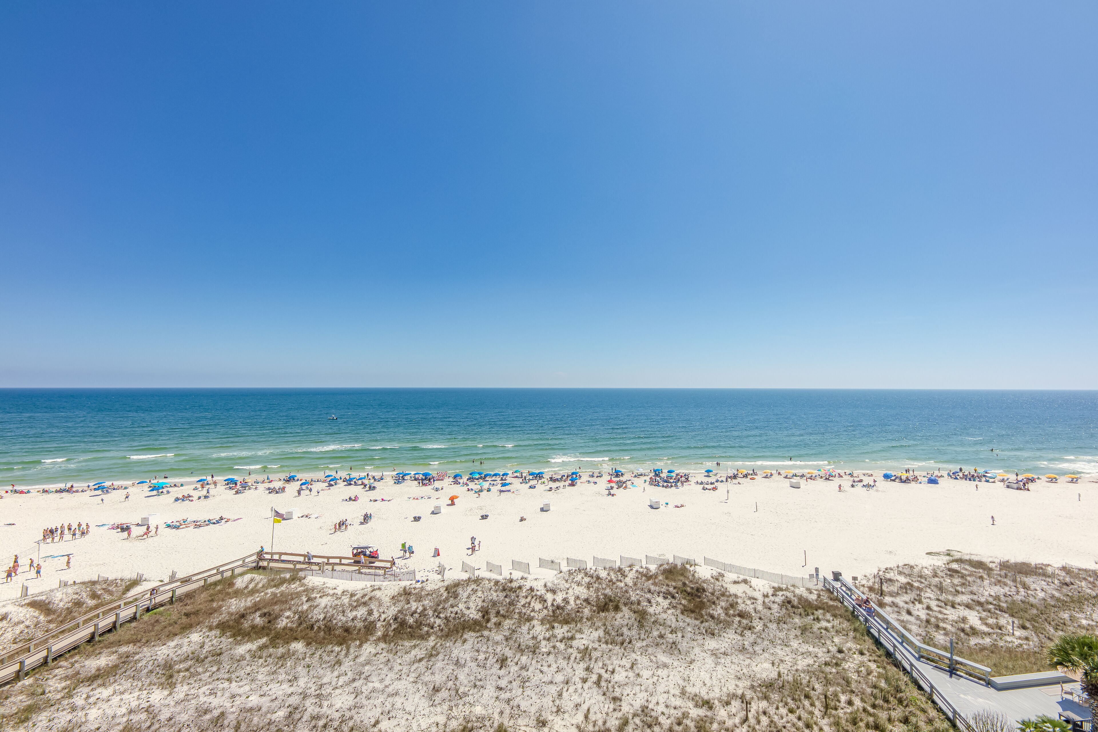 A beach with a wooden boardwalk leading to the shore, sandy beach, and clear blue sky.