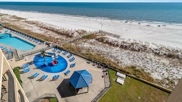 A resort with a swimming pool, sun loungers, and a beach view.